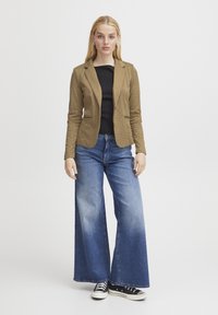 Rutig brun kavaj med en figurnära design, svart topp, vida utblekta blå jeans och svarta sneakers. Släta texturer genom hela outfiten.