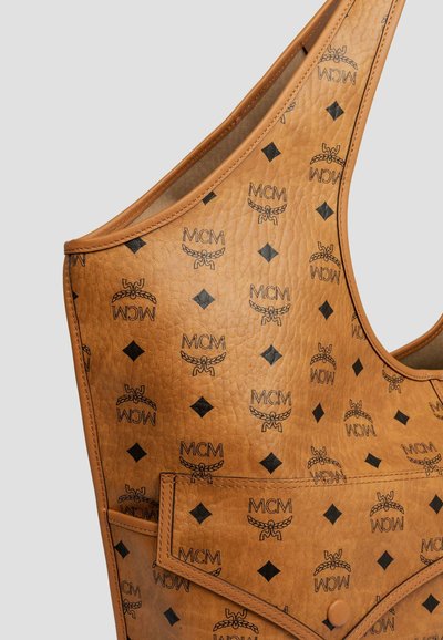 Tan färgad läderaxelväska med svarta MCM-logotyper och diamantformer, som har en framficka med tryckknappslås.