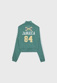 Giacca verde con strisce bianche sulle maniche, caratterizzata da una bandiera giamaicana gialla e nera, il testo "JAMAICA" e il numero "84" sulla schiena.