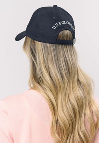 Șapcă bleumarin cu text brodat alb „U.S. POLO ASSN.” Curea reglabilă în spate, material din bumbac, design structurat.