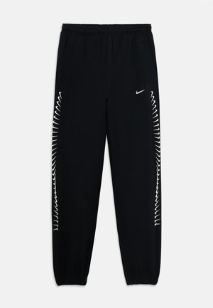 Fekete Nike melegítőnadrág, elasztikus derékkal, oldalsó zsebekkel és fehér cikk-cakk mintázattal a külső varratok mentén. Bemelegítő pántok a bokán.