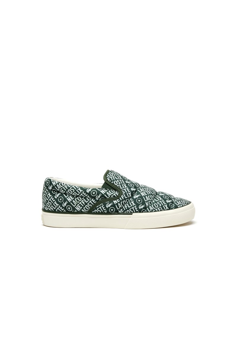 Gröna slip-on sneakers med vit text och mönster, med gummisula och textilöverdel. Minimalistisk design utan synliga snören.