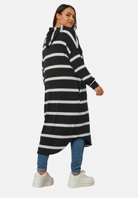 Mustat ja harmaat raidalliset hupparikauluksella varustetut neuletakit, pitkät hihat, sivuleikkaukset ja rento malli, yhdistettyinä sinisiin farkkuihin ja valkoisiin lenkkareihin.