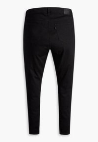 Jean skinny noir posé à plat montrant le dos avec deux poches, passants de ceinture et un patch de marque en cuir sur la ceinture.