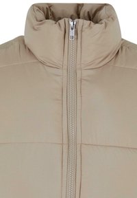 Beige pufferjack met een hoge, geplooide kraag en een volledige ritssluiting. Glad stof met horizontale stiksels voor isolatie.