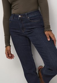 Jean en denim bleu foncé avec une coupe droite classique, comportant cinq poches, une fermeture à bouton en métal et des coutures contrastées.