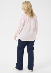 Blusa rosa chiaro, con texture, maniche a sbuffo, piega sul retro e orlo arrotondato, abbinata a jeans blu scuro e sneakers beige chiaro.
