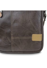 Bolso de cuero marrón con superficie texturizada, con costuras en color beige y una etiqueta de logotipo en relieve. Forma rectangular, construcción resistente.