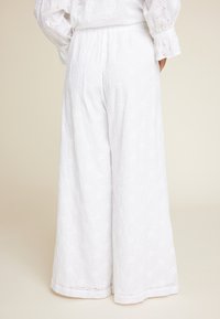 Bredde ben hvite bukser laget av teksturert stoff med eyelet broderi. Har strikk i livet og subtil søm langs kanten.