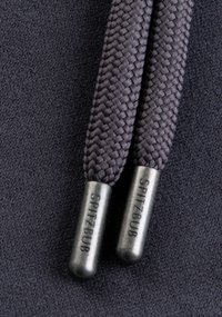 Grijze gevlochten veters met metalen uiteinden met het label "SPITZBUB," rustend op een donkere stoffonde. De textuur lijkt glad en geweven.