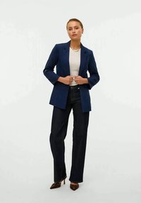 Marineblazer med en skreddersydd design, notklapper og lange ermer, paret med tettsittende mørke jeans og spisse hæler.