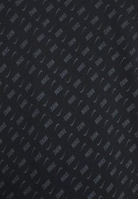 Svart tyg med ett upprepat mönster av grå Nike-logotyper och swooshar, vilket skapar en texturerad, subtil design. Mjuk material.