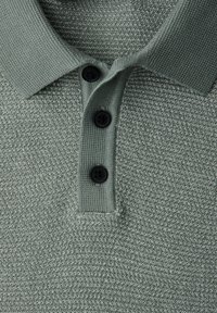 Polo en tissu texturé vert clair, doté d'un col et de trois boutons noirs centrés.