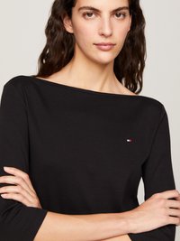 Svart langermet topp med bred utringning. Har en liten farget logo på brystet. Glatt tekstur og tettsittende design.