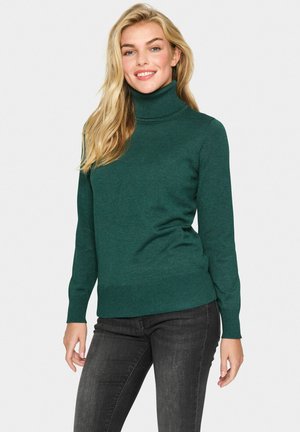 Green turtleneck sweater made of soft knit fabric, featuring a fitted design, ribbed cuffs, and hem. Paired with dark jeans.