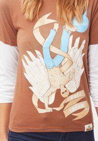 Camiseta de algodón marrón con un diseño gráfico de una figura con alas, pantalones azules y una cinta, con el texto "vale caelum" en acentos crema.