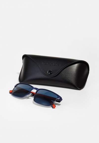 Granatowe okulary przeciwsłoneczne z przyciemnianymi soczewkami i czerwonymi akcentami, w parze z czarną skórzaną etui z zapięciem na napę i wytłoczonym logo.