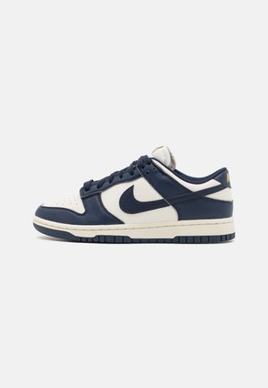 Sneaker Nike Dunk Low avec une tige en cuir bleu marine, une boîte à orteils de couleur crème et une semelle en caoutchouc texturée. Comprend un Swoosh bleu marine et des accents de marque.