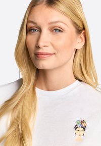 White cotton t-shirt featuring a colorful embroidered design of a female figure with floral accents on the head, displayed at the left chest.