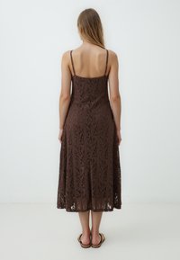 Abito maxi marrone in pizzo con spalline regolabili e una silhouette ampia, caratterizzato da intricati motivi e una texture liscia.