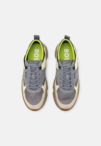 Baskets avec une tige en mesh gris et des accents crème, une semelle arrondie couleur tan, une semelle intérieure verte avec l'inscription "BOSS" et des lacets gris.