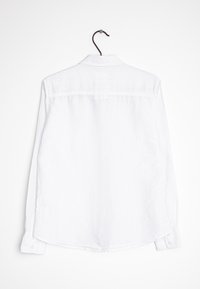 Vit långärmad skjorta med knapp-ned krage och subtila vertikala ränder. Har en rak nederkant och knappade ärmslut. Hänger på en svart krok.