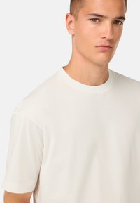 Krämfärgad kortärmad t-shirt med rundad hals, tillverkad av mjukt tyg, med avslappnad passform och slät textur.