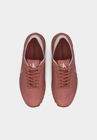 Ζευγάρι σκόπιων ροζ αθλητικών παπουτσιών Calvin Klein με κορδόνια, λευκή περίμετρο και σόλες χρώματος καραμέλας, από ψηλά σε λευκό φόντο.