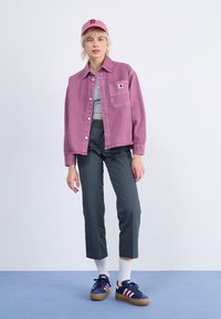 Rosa denimjacka över en grå topp, ihop med mörkgrå cropped byxor och marinblå sneakers med rosa ränder. Accessoriserad med en rosa keps.