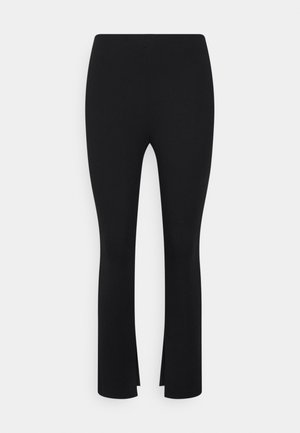 Schwarze Leggings mit einem ausgestellten Design, die am unteren Ende Schlitze aufweisen. Hergestellt aus dehnbarem Material, mit glatter Textur und ohne sichtbare Muster.