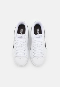Baskets blanches de sport avec des accents latéraux noirs, design à lacets, matériau synthétique texturé et logo "PUMA" sur la languette.