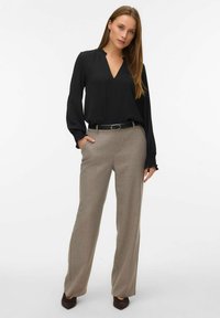 Melna blūze ar V veida kakla izgriezumu un garām piedurknēm, kombinēta ar gaiši bežām biksēm un melnu jostu. Bikses ir taisna griezuma.