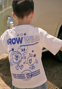 Witte katoenen t-shirt met een blauw grafisch ontwerp met cartoonfiguren, tekst "GROW WILD" en verschillende speelse vormen en accenten.