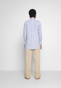 Randig skjorta i blått och vitt med längre bakstycke, vida ärmar och avslappnad passform, parat med ljusbeiga vida byxor.