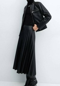 Veste en cuir noir avec des zips argentés, associée à une jupe plissée noire et des bottes noires jusqu'aux genoux. Texture lisse et design ajusté.