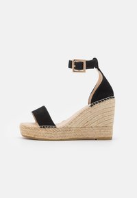 Black suede wedge sandal with open toe design, adjustable ankle strap, and jute-wrapped platform. Textured surface and minimalist style.
