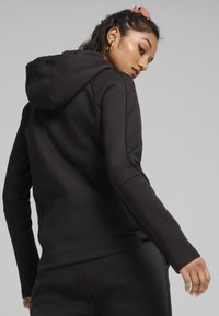 Sudadera con capucha negra de manga larga, con tela texturizada en los lados y un corte relajado. Costuras visibles y detalles acanalados en los puños.