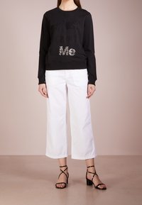 Svart sweatshirt med präglad "#JustCavalliMe" text, vita vida byxor och svarta klacksandaler med remmar. Slät tygkvalitet och avslappnad passform.