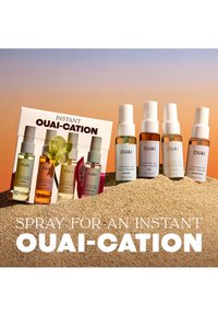 Quatre flacons de brume parfumée Ouai et leur boîte exposés sur le sable contre un ciel au coucher du soleil avec le texte "Spray for an instant OUAI-CATION."