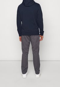 Marinblå hoodie i bomull med kenguruficka och ribbade ärmslut, kombinerad med grå byxor och vita sneakers.