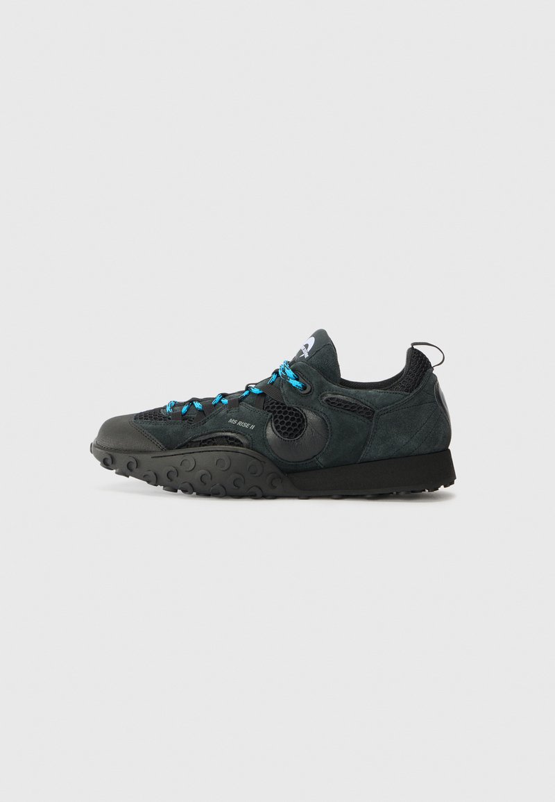 Black suede and mesh athletic shoe with blue laces, rounded toe, and textured rubber sole featuring circular patterns. Side profile view.