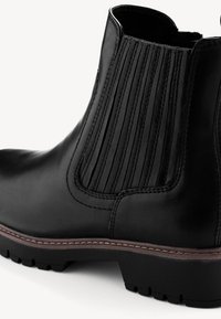 Bota de cuero negro hasta el tobillo con paneles elásticos acanalados, parte superior texturizada, costuras marrones contrastantes y una suela rugosa para tracción.