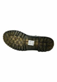 Suela de goma negra con surcos profundos, que presenta una superficie texturizada y una pequeña etiqueta de instrucciones de cuidado adjunta cerca del talón.