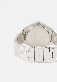 Montre en acier inoxydable argenté avec un bracelet à maillons, présentant un boîtier rond et une finition polie, avec un logo gravé sur le fermoir.
