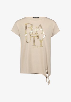 T-shirt beige à manches courtes avec le texte "BEAUTY" doré brillant à l'avant et un détail de nœud noué sur l'ourlet inférieur droit.