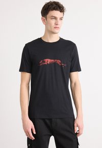 Svart bomull T-skjorte med et rødt grafisk motiv av en hoppende greyhound på brystet. Korte ermer og rund hals. Myk tekstur.