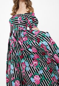 Robe florale décolletée avec un motif rayé noir et blanc, ornée de roses roses et de fleurs bleues, en tissu texturé, avec une jupe fluide.