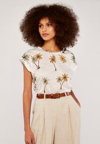 White short-sleeved top featuring a palm tree print in green and brown, paired with beige high-waisted trousers and a brown belt.
