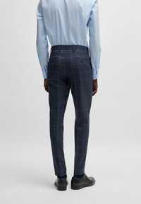 Pantaloni a quadri blu navy con vestibilità slim, dotati di tasche laterali, tasche posteriori con bottoni e una texture del tessuto liscia. Abbinati a scarpe nere.