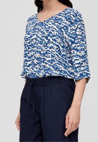 Top blu e bianco con motivo a fantasia, scollatura a V e maniche a tre quarti, abbinato a pantaloni navy con vita elastica. Tessuto morbido e strutturato.